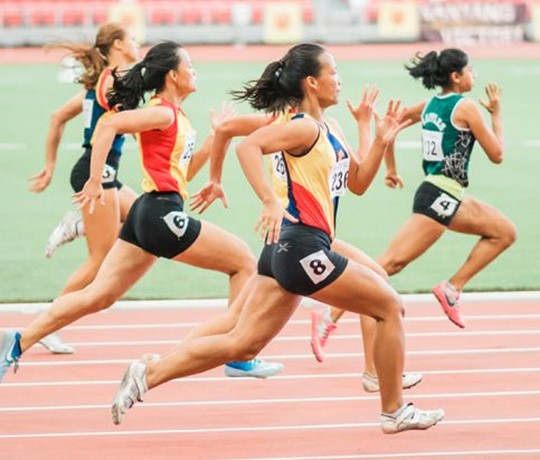 Five women running on an athletics track. The view is from the side as the runners go past.