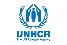 The UNHCR logo - a blue pair of hands shelters a cartoon person, surrounded by a wreath, underneath which there is the blue text 'The UN Refugee Agency'.
