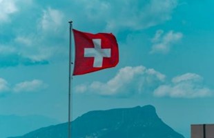Bandera suiza contra el cielo nublado azul brillante.